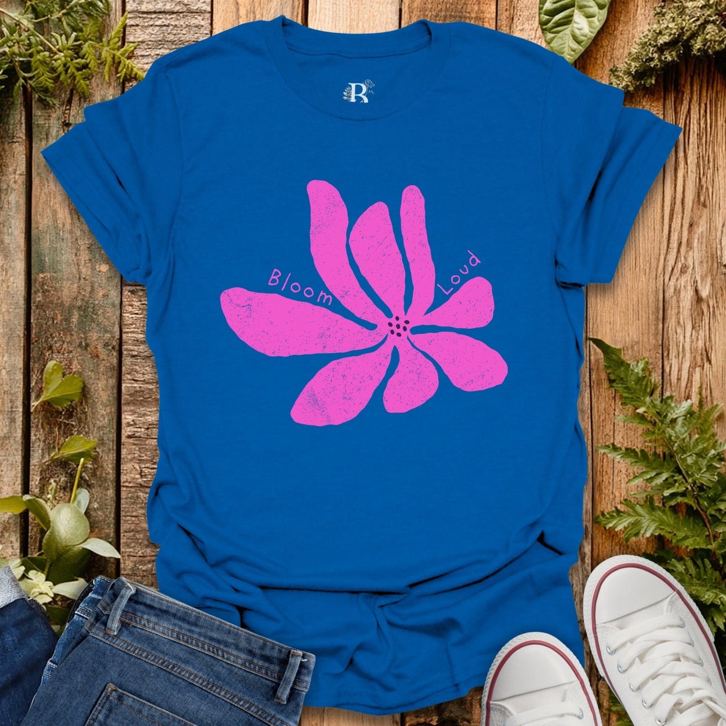 Blue t-shirt with pink flower graphic and text on a wooden surface with plants.