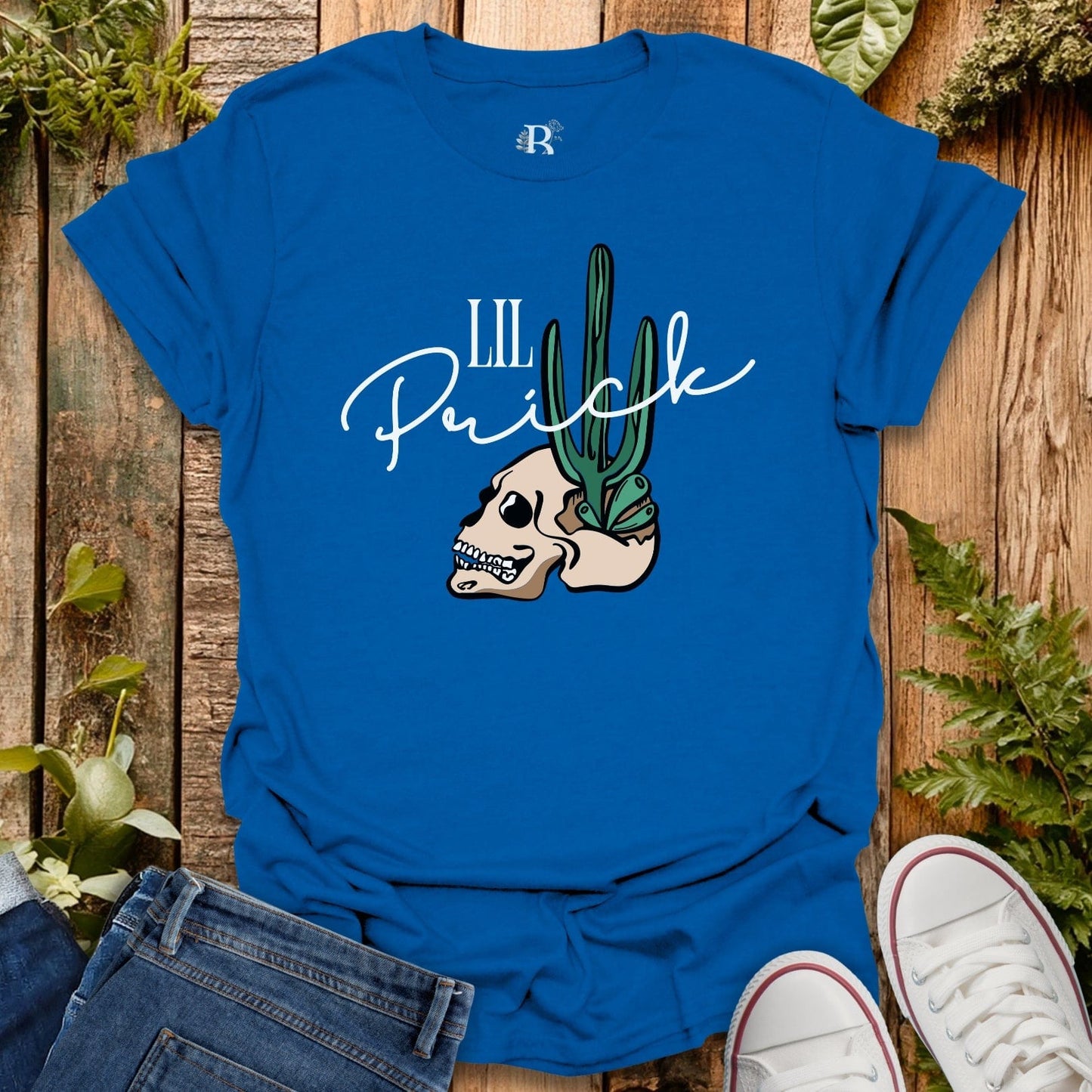 Blue t-shirt with skull and cactus design on a wooden surface with plants.
