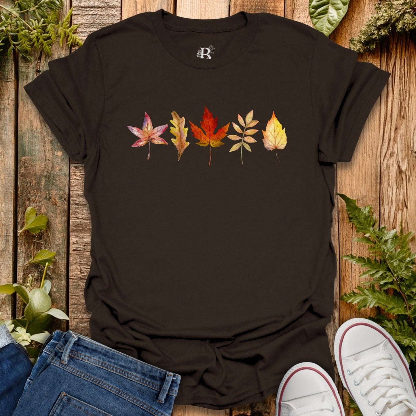 Black t-shirt with colorful leaf design on a wooden surface with plants.