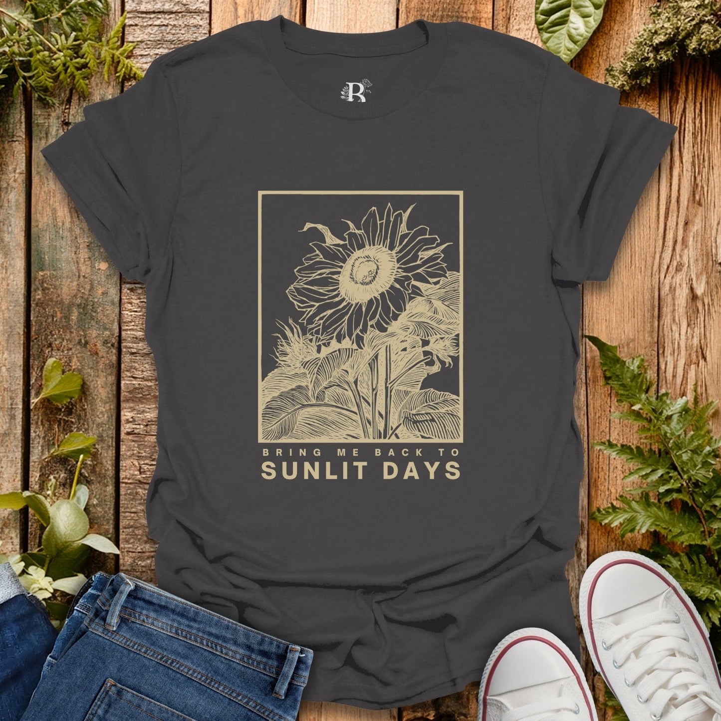 Black t-shirt with sunflower design and text on a wooden surface with plants.