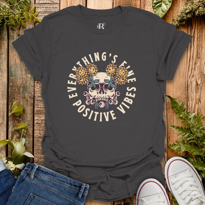 Black t-shirt with skull and sunflower design on a wooden surface with jeans and sneakers.