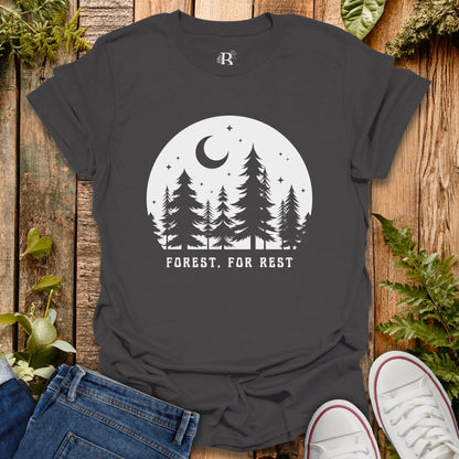 Black t-shirt with forest design and 'Forest, For Rest' text on a wooden surface with plants.