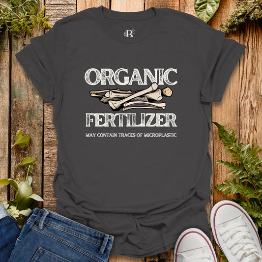Black t-shirt with 'Organic Fertilizer' graphic on a wooden background with plants.