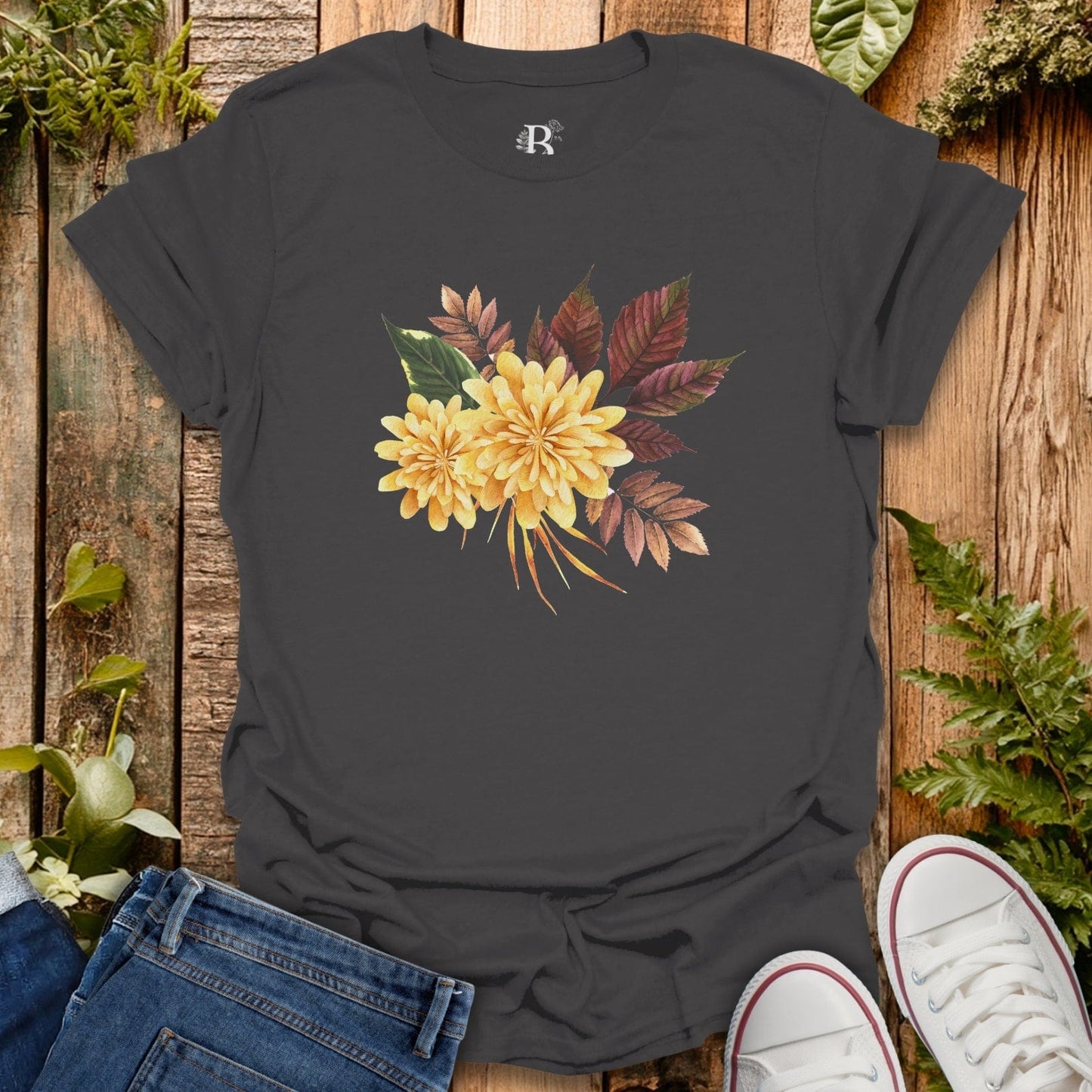 Black t-shirt with yellow floral design on a wooden surface with jeans and sneakers.