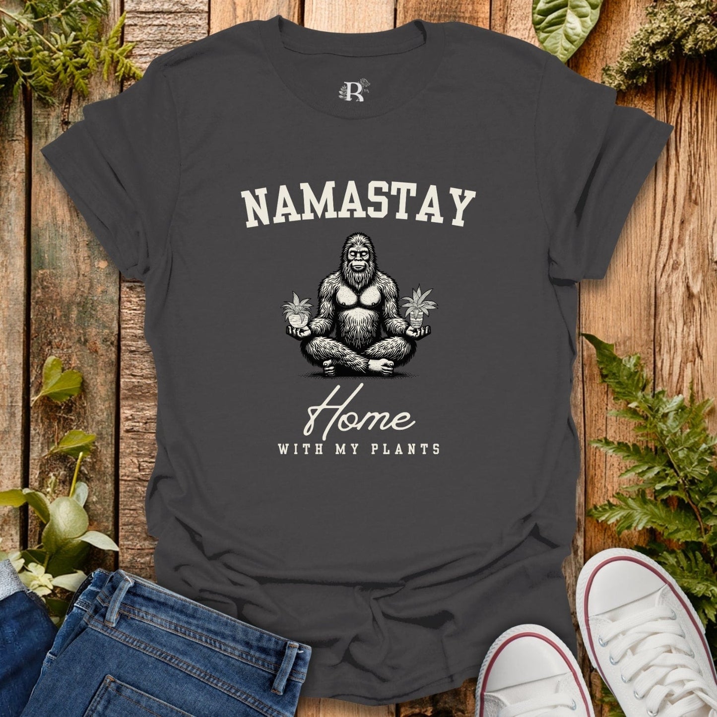 Black t-shirt with 'Namastay Home with My Plants' design on a wooden background with plants.