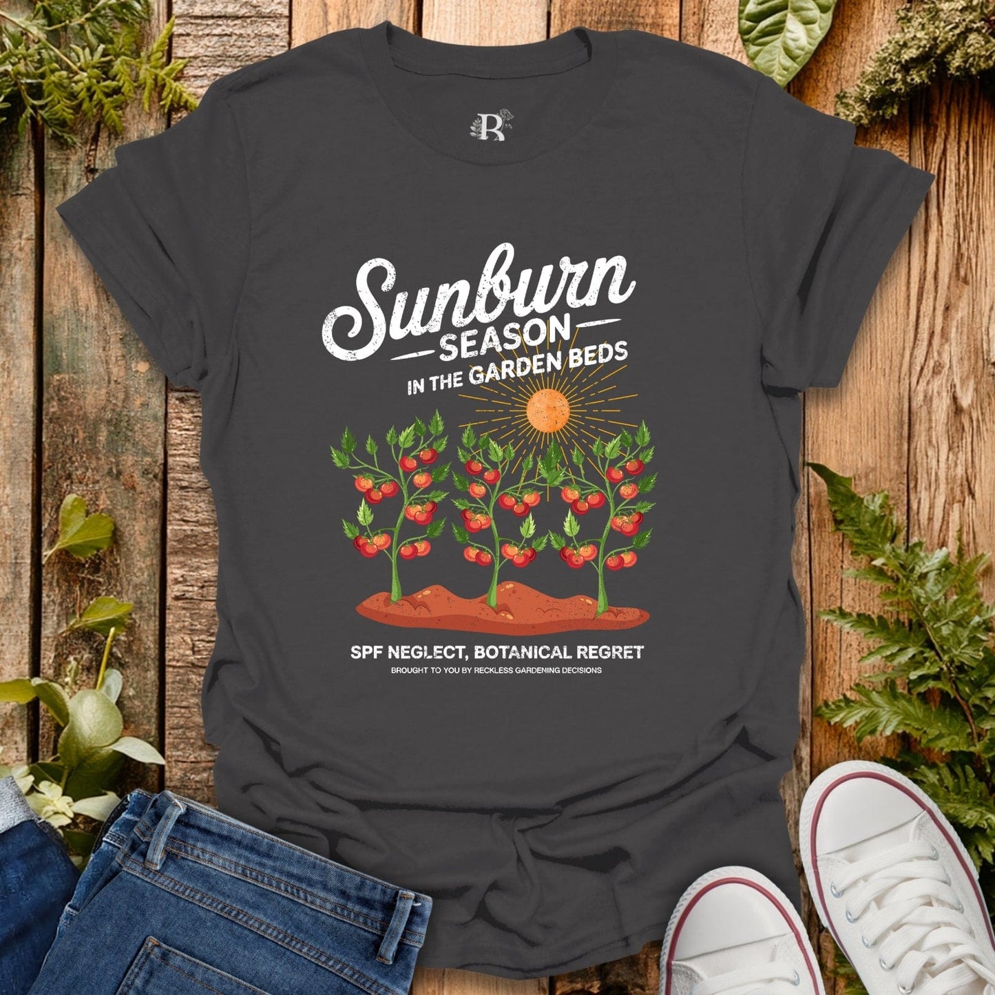 Black t-shirt with garden-themed design on a wooden surface with plants and shoes.