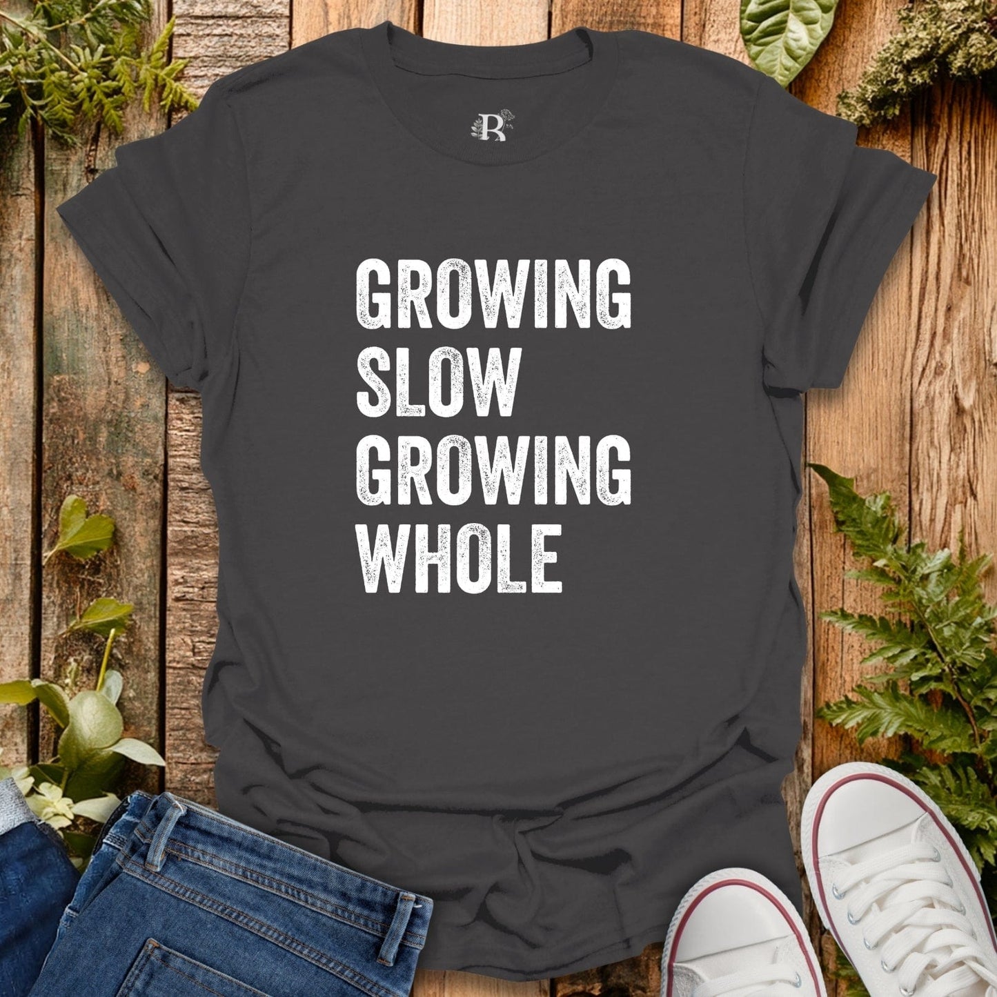 Black t-shirt with 'GROWING SLOW GROWING WHOLE' text on a wooden surface with plants.