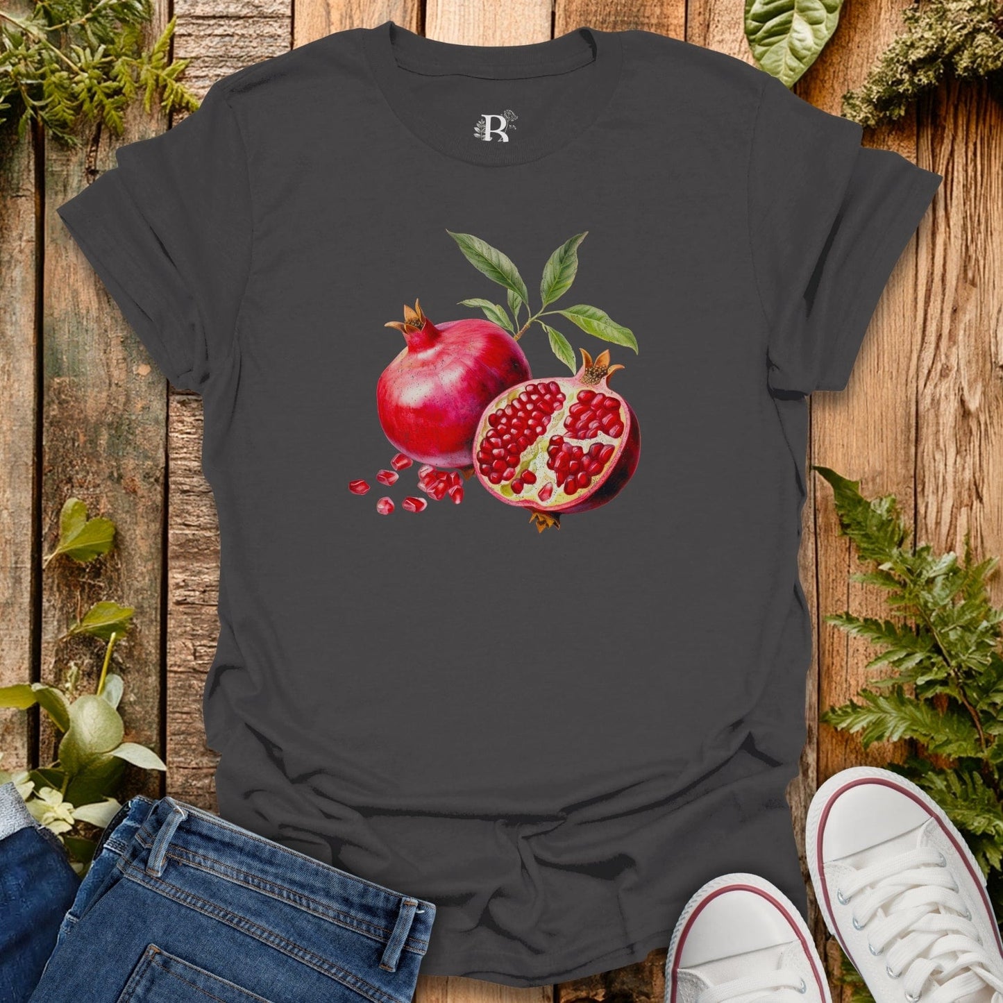 Black t-shirt with pomegranate design on a wooden surface with plants.