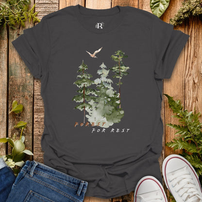 Dark gray t-shirt with forest design and 'Forest for Rest' text on a wooden surface with plants.