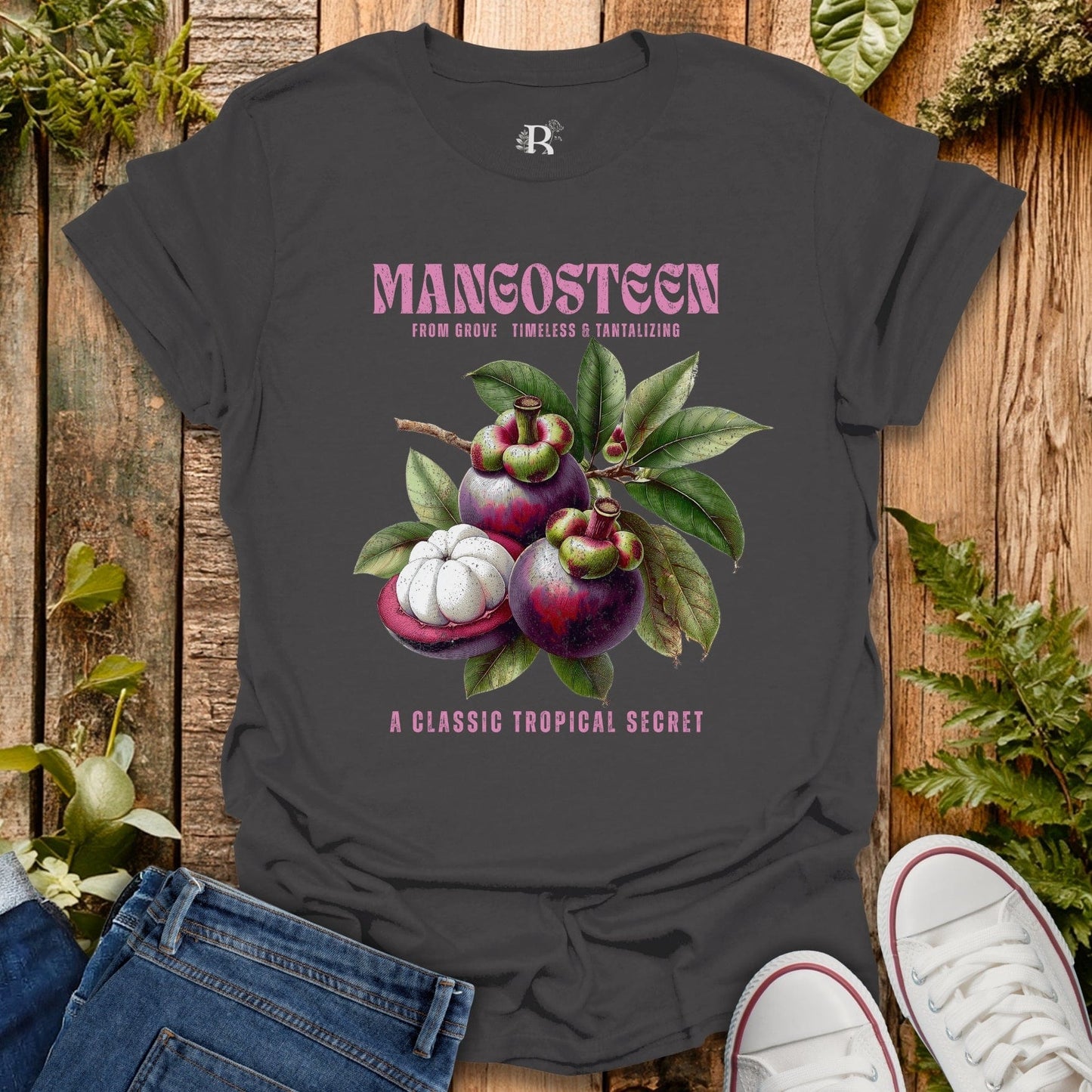 Dark gray t-shirt with mangosteen graphic and text on a wooden surface with plants.