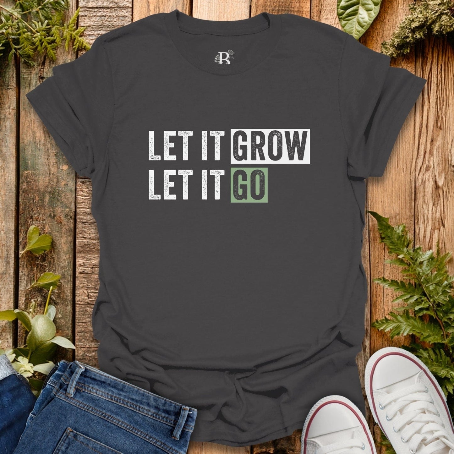Black t-shirt with 'LET IT GROW LET IT GO' text on a wooden surface with plants.