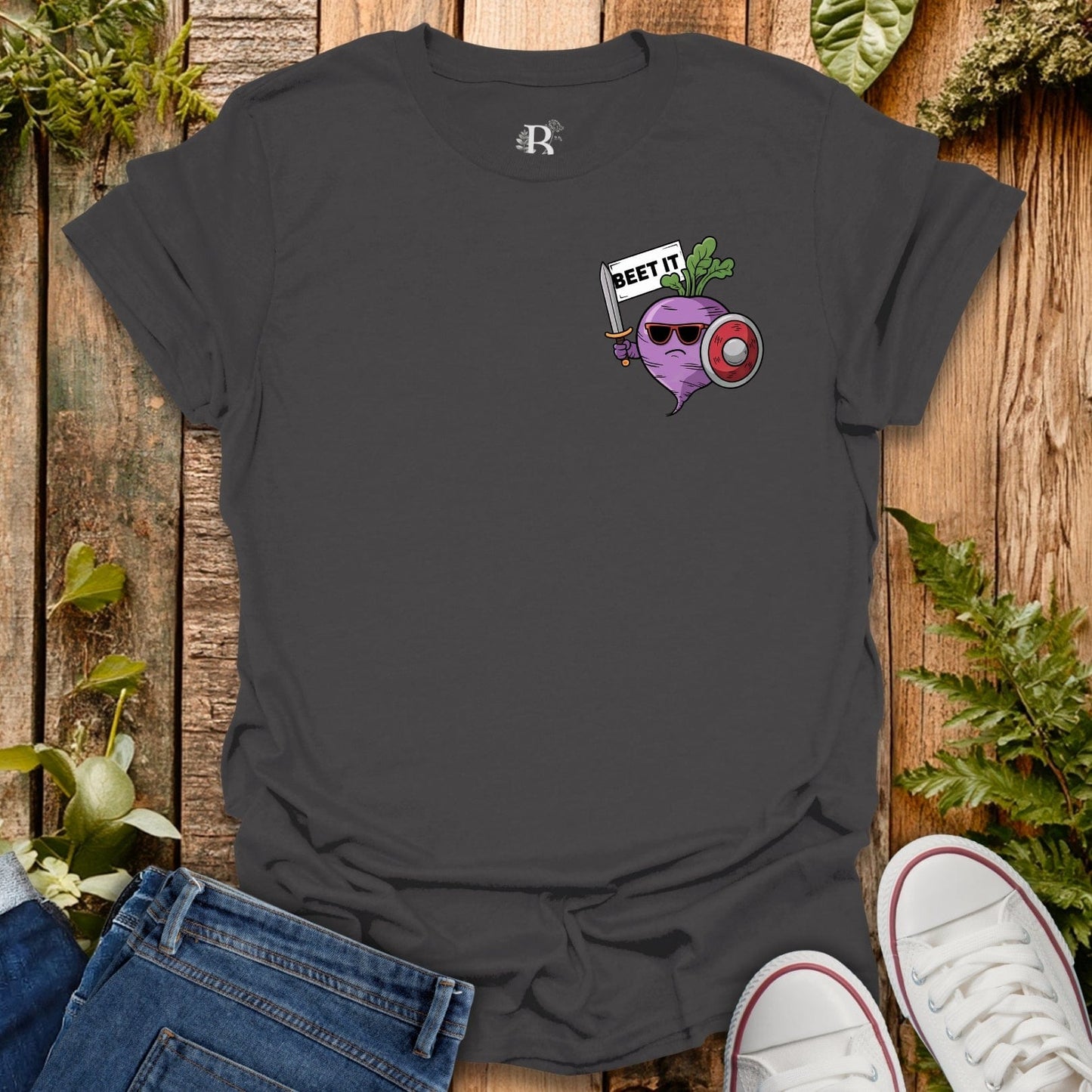 Black t-shirt with graphic design on a wooden surface with jeans and sneakers.