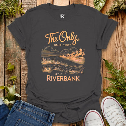 Black t-shirt with nature-themed design and text on a wooden surface with jeans and shoes.