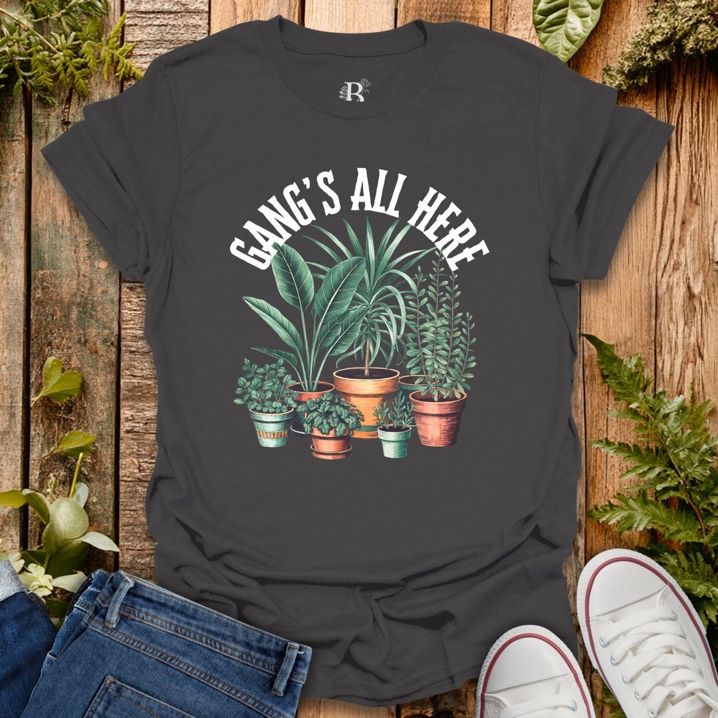 Black t-shirt with plant graphic and 'Gang's All Here' text on a wooden surface with plants.