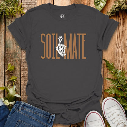 Black t-shirt with 'SOIL MATE' design on a wooden surface with jeans and sneakers.