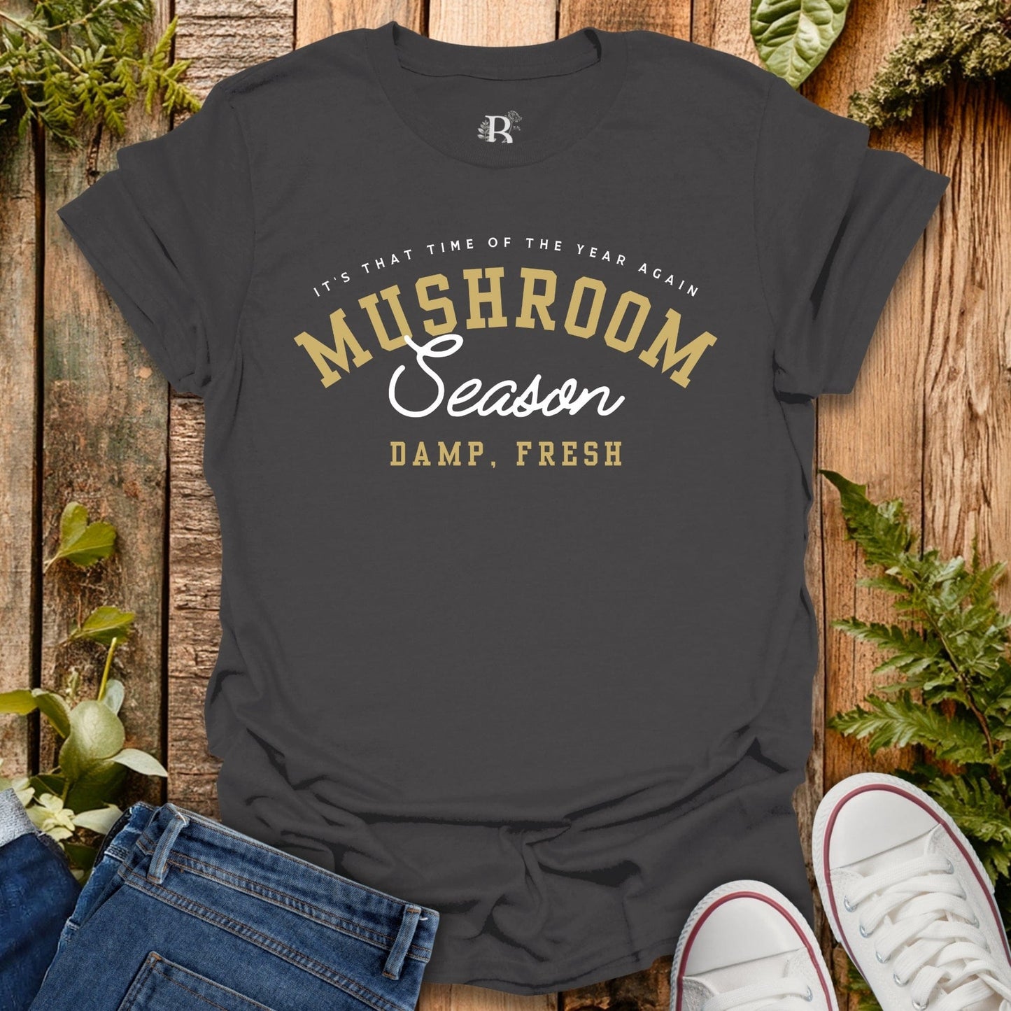Dark gray t-shirt with 'Mushroom Season' text on a wooden surface with plants.