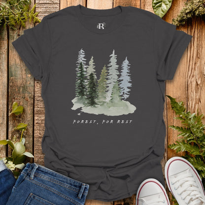 Dark gray t-shirt with forest graphic and 'Forest, For Rest' text on a wooden surface with plants.