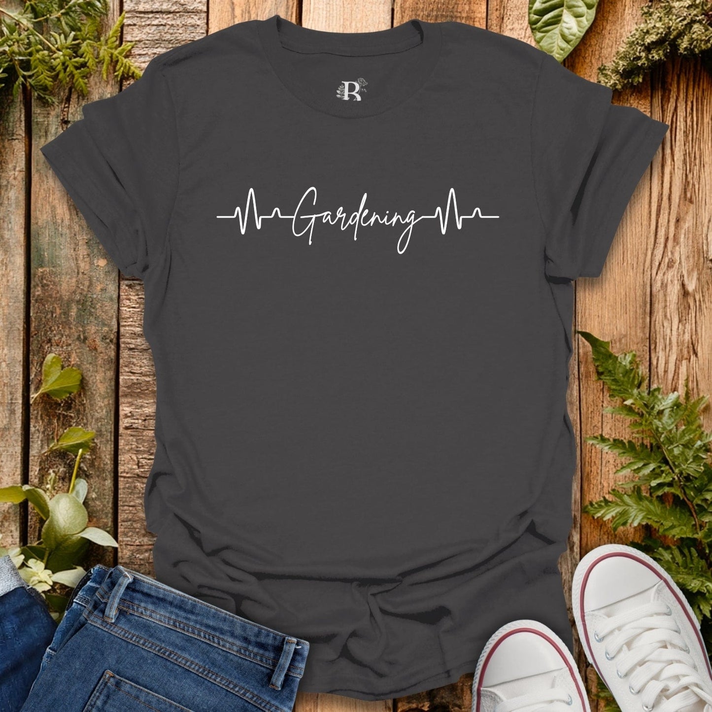 Black t-shirt with 'Gardening Heartbeat' text on a wooden surface with plants.