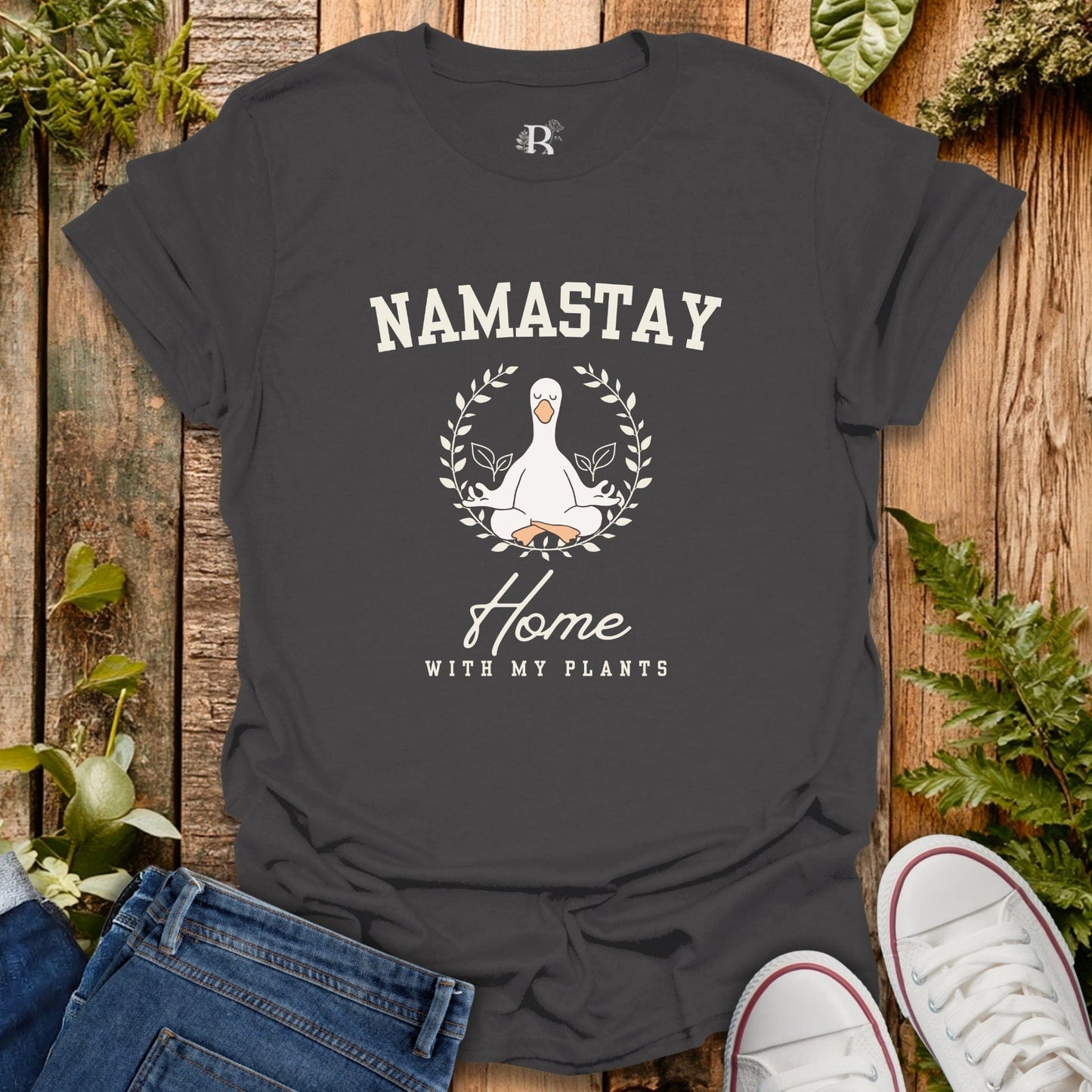 Black t-shirt with 'Namastay Home with My Plants' design on a wooden surface with plants.