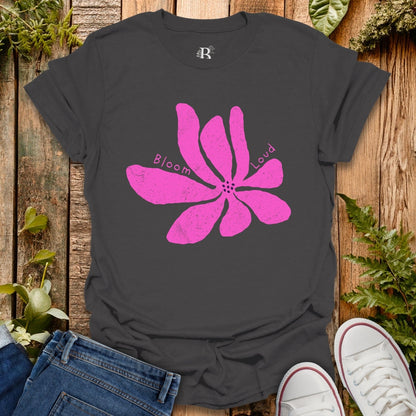 Black t-shirt with a pink flower graphic and text on a wooden surface with jeans and sneakers.
