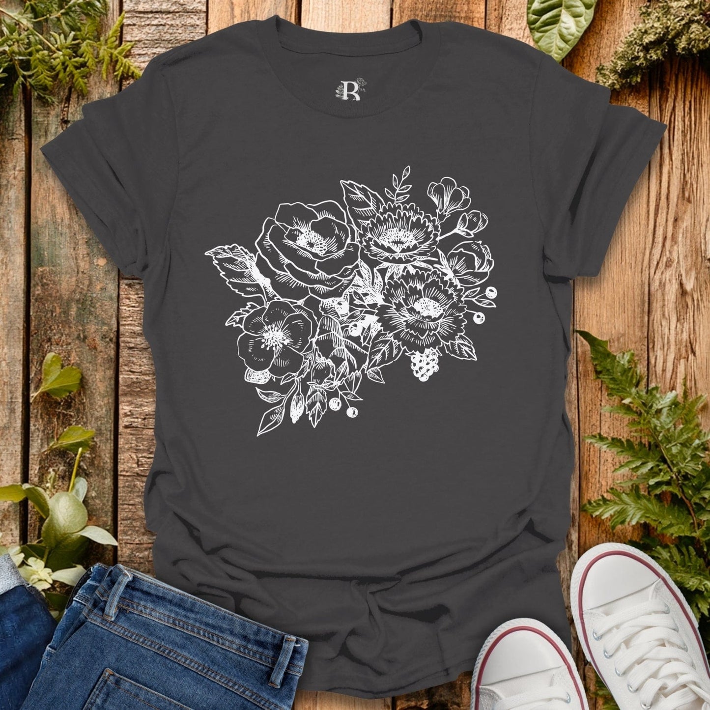 Black t-shirt with floral design on a wooden surface with jeans and sneakers.