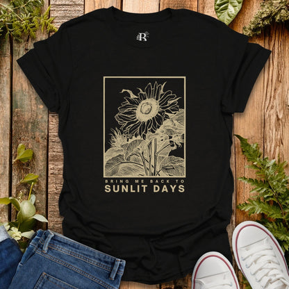 Black t-shirt with sunflower design and text on a wooden surface with plants.