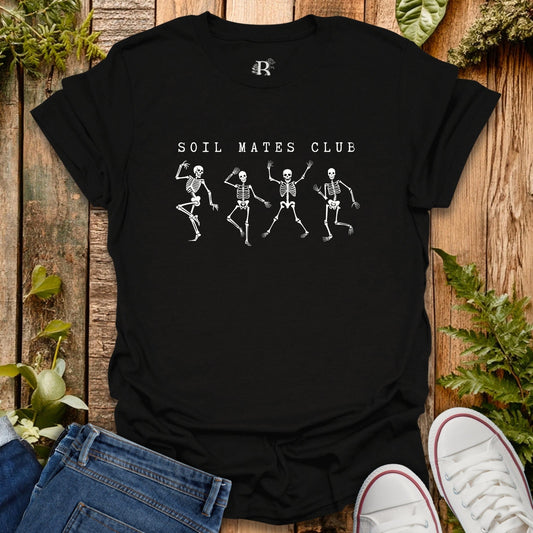 Black t-shirt with skeleton design and 'Soil Mates Club' text on a wooden surface with plants.