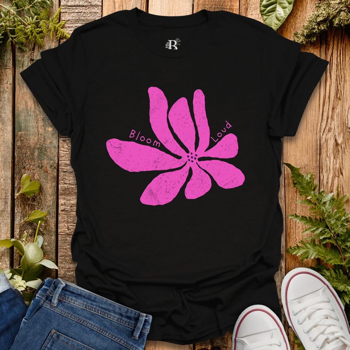Black t-shirt with a pink flower graphic and text on a wooden surface with plants.