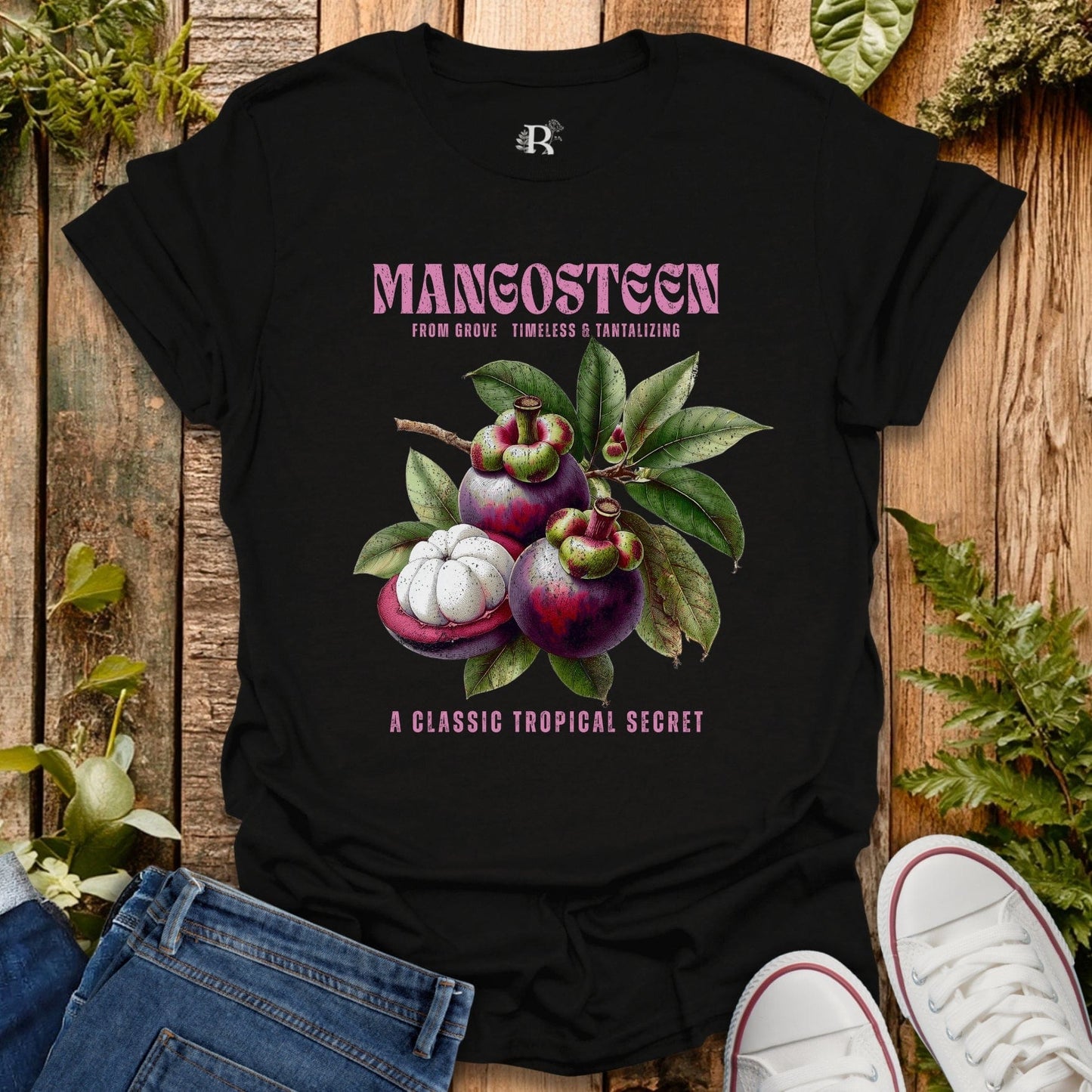 Black t-shirt with mangosteen graphic and text on a wooden surface with plants.