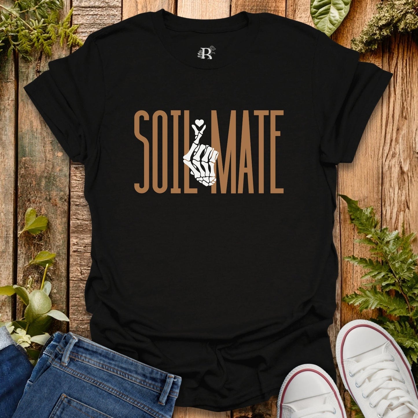 Black t-shirt with 'SOIL MATE' text and graphic on a wooden surface with plants.