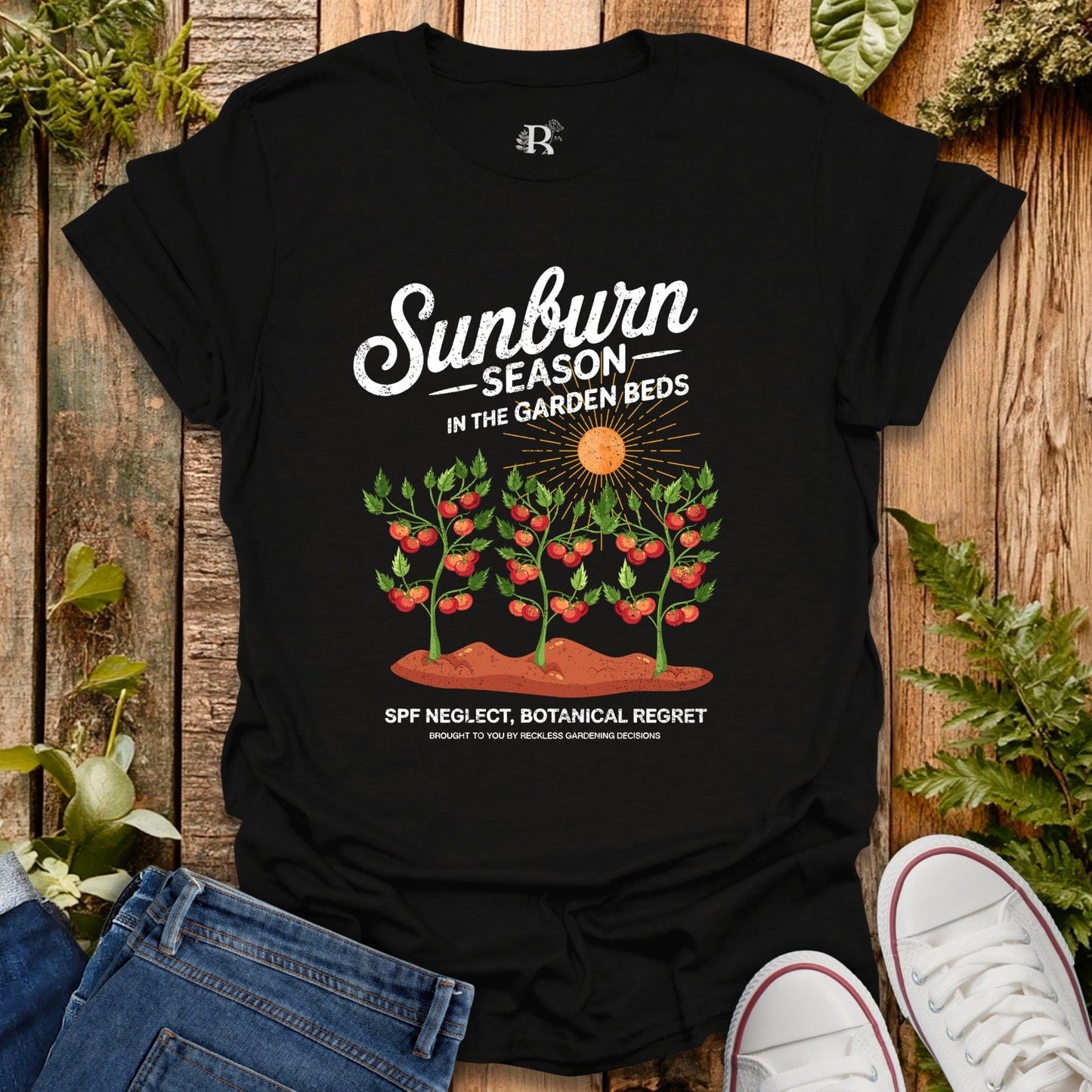 Black t-shirt with garden-themed design on a wooden surface with plants.