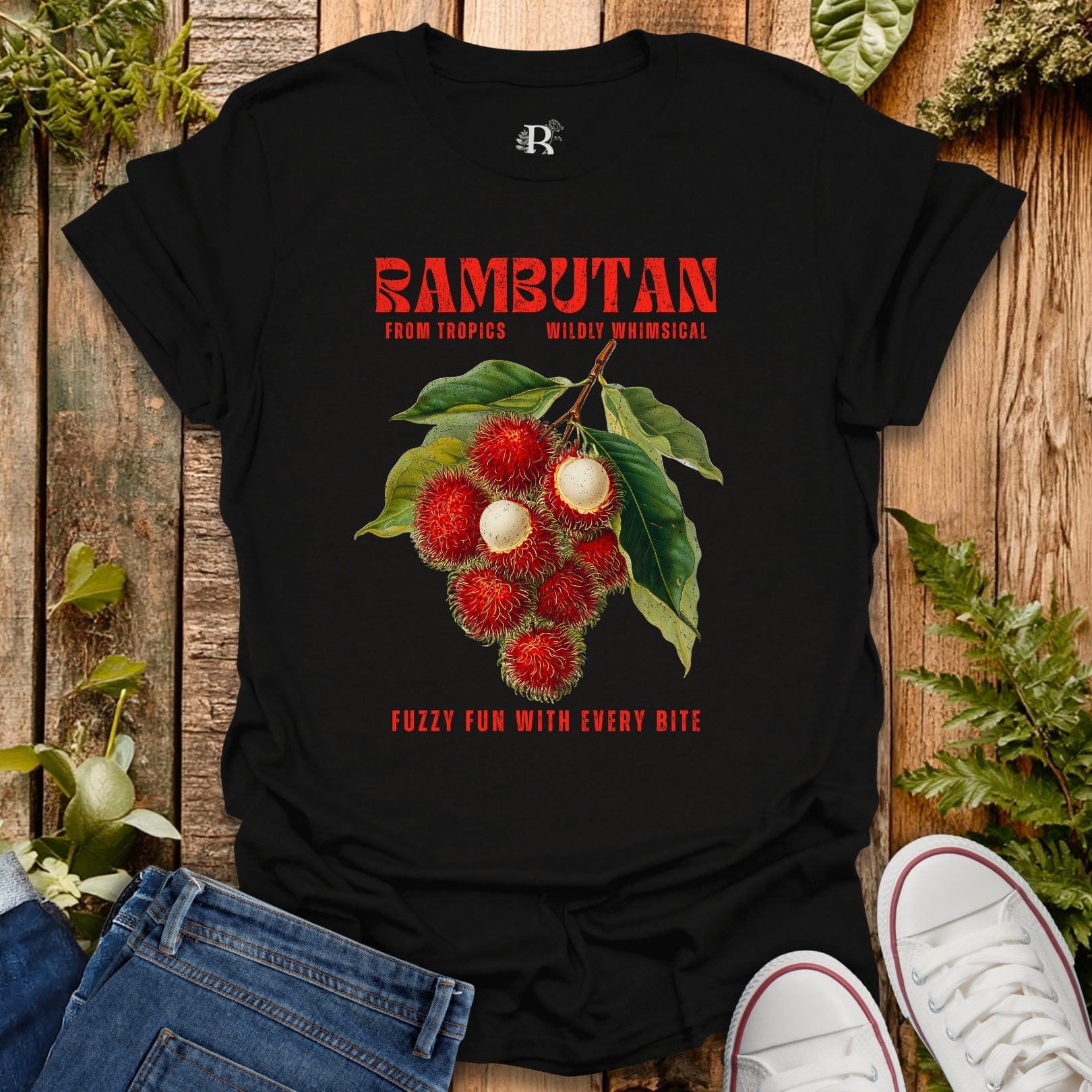 Black t-shirt with rambutan graphic and text on a wooden surface with plants.