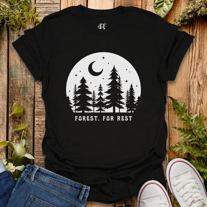 Black t-shirt with 'Forest. For Rest' design on a wooden surface with plants.