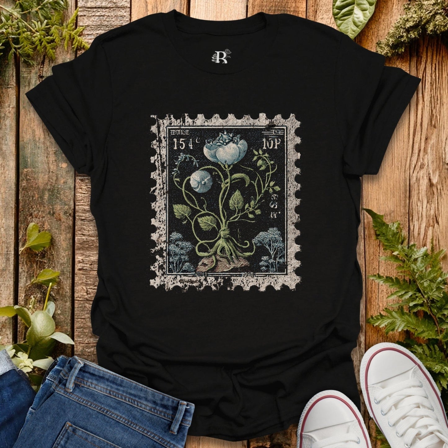 Black t-shirt with vintage-style floral design on a wooden surface with plants.
