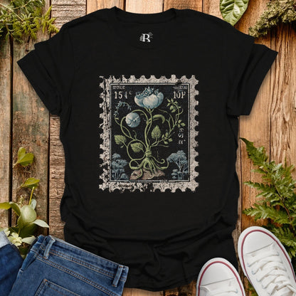 Black t-shirt with vintage-style floral design on a wooden surface with plants.