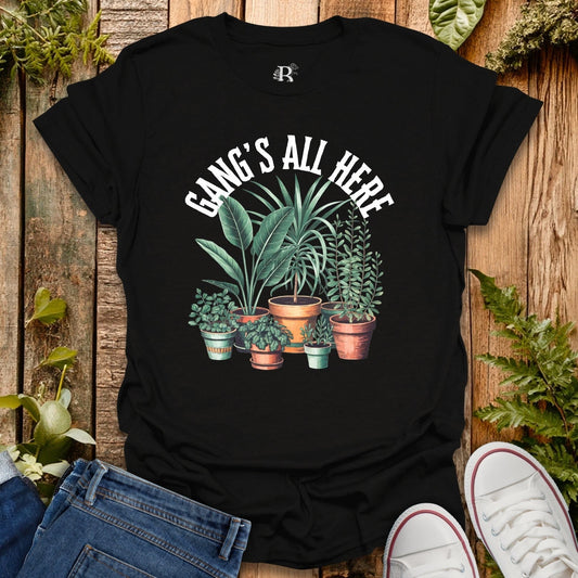 Black t-shirt with plant design and 'Gang's All Here' text on a wooden background