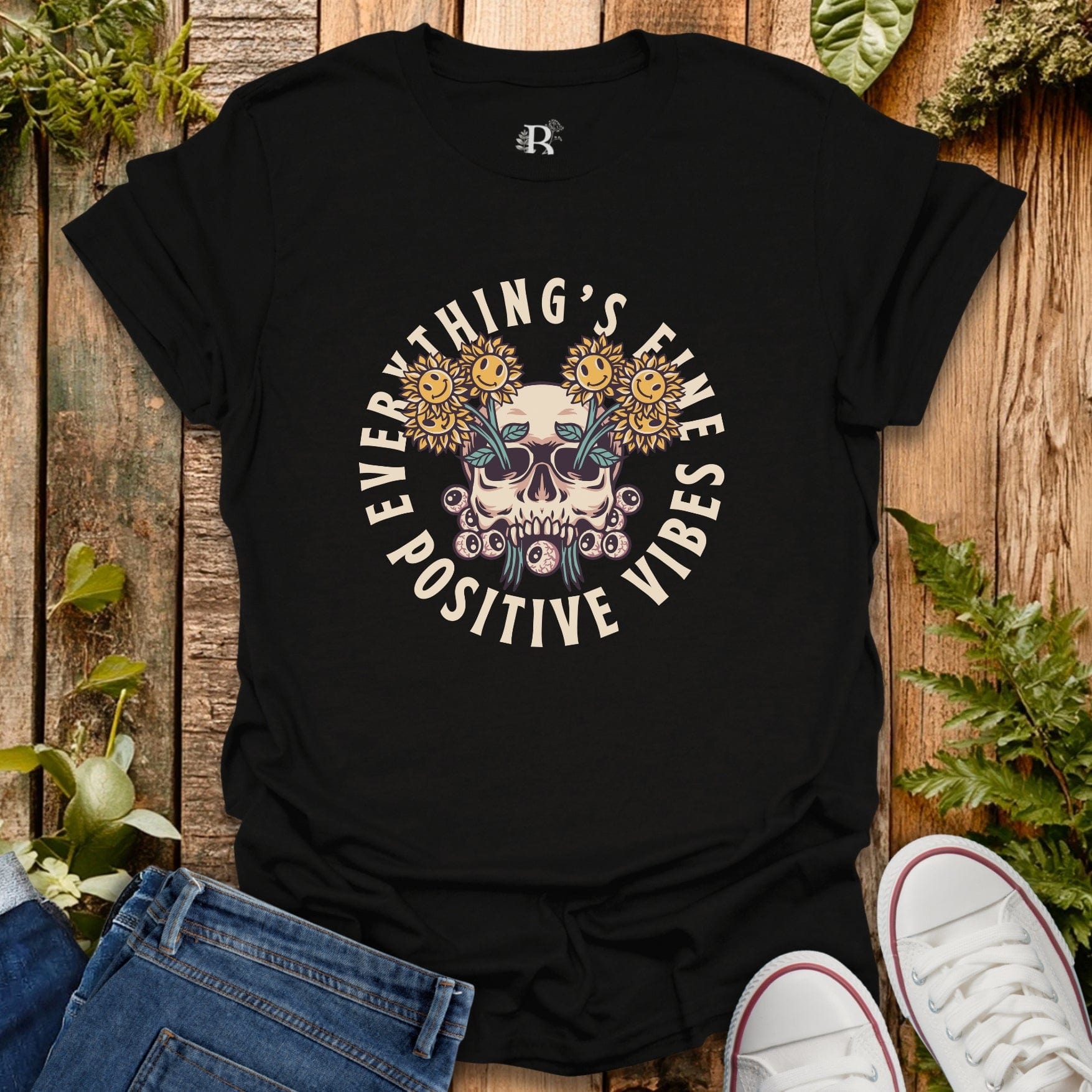 Black t-shirt with skull and sunflower design on a wooden surface with jeans and sneakers.