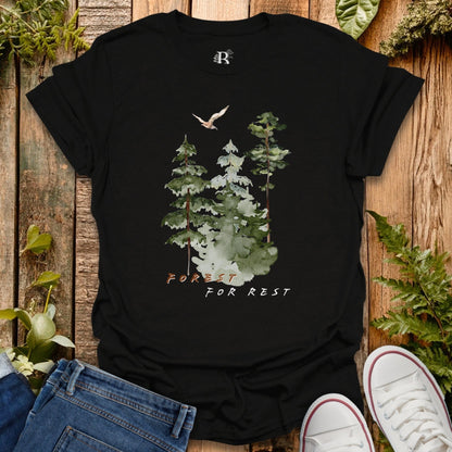 Black t-shirt with forest design and text 'Forest for Rest' on a wooden surface with plants.