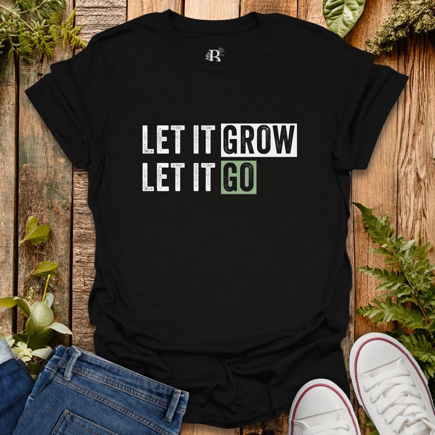Black t-shirt with 'LET IT GROW LET IT GO' text on a wooden surface with plants.