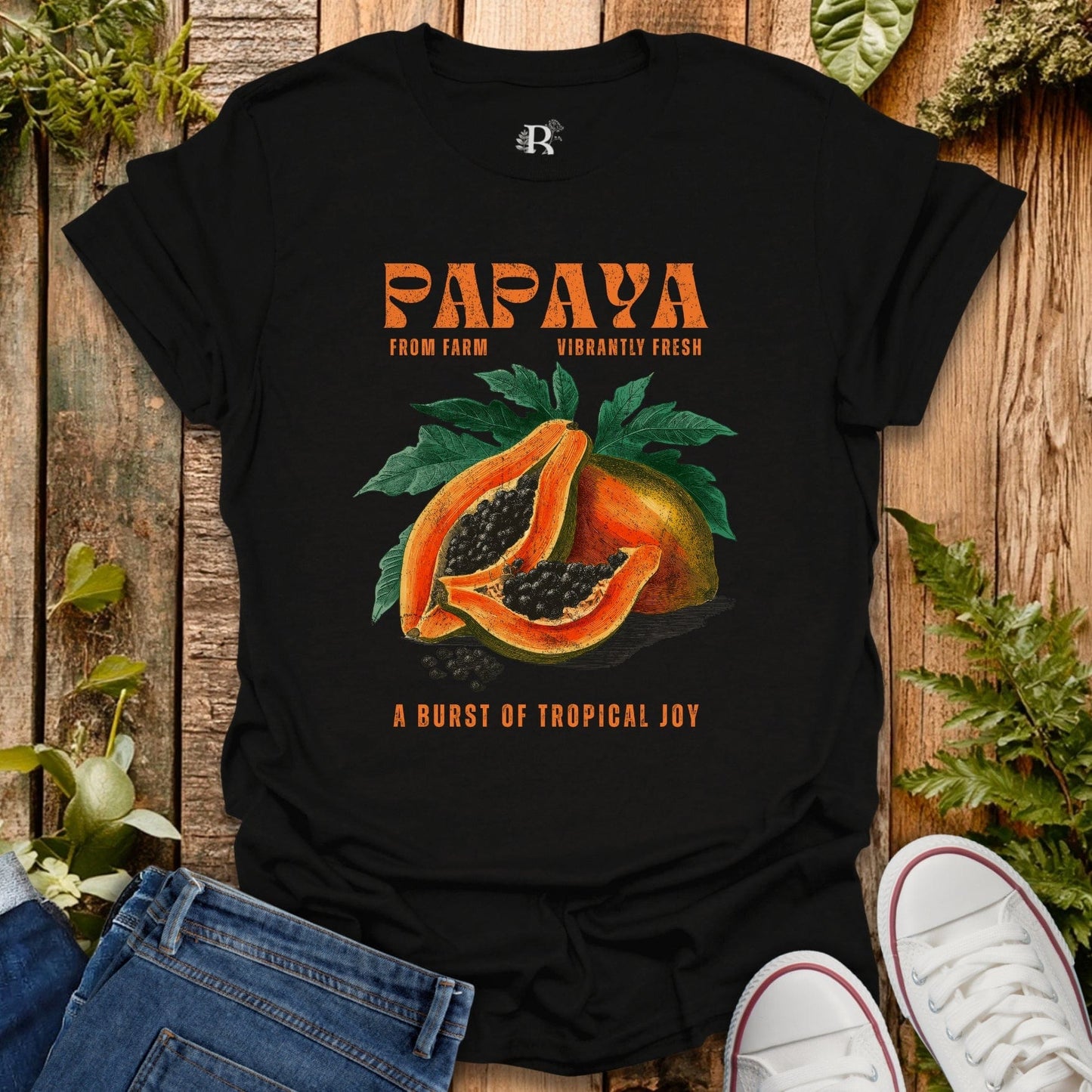 Black t-shirt with papaya graphic and text on a wooden surface with plants.