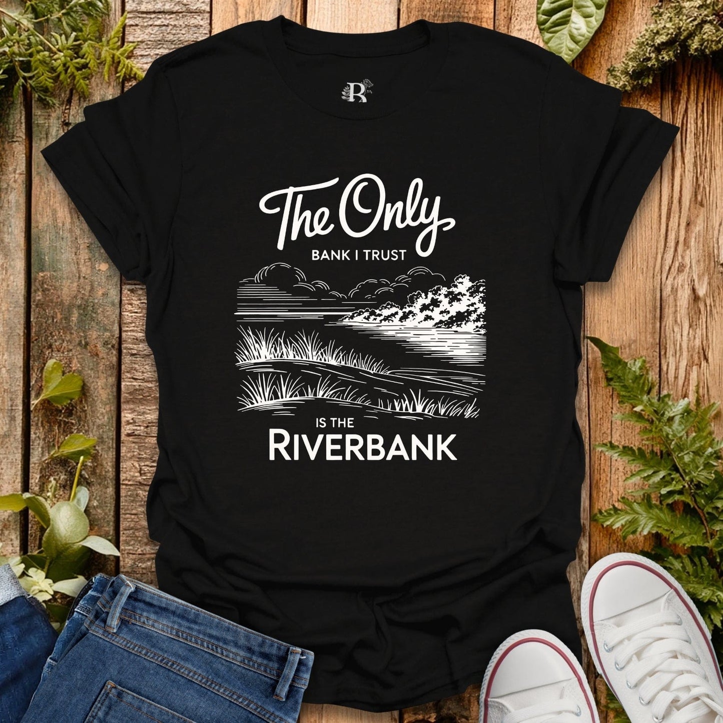 Black t-shirt with nature-themed design and text on a wooden surface with plants.