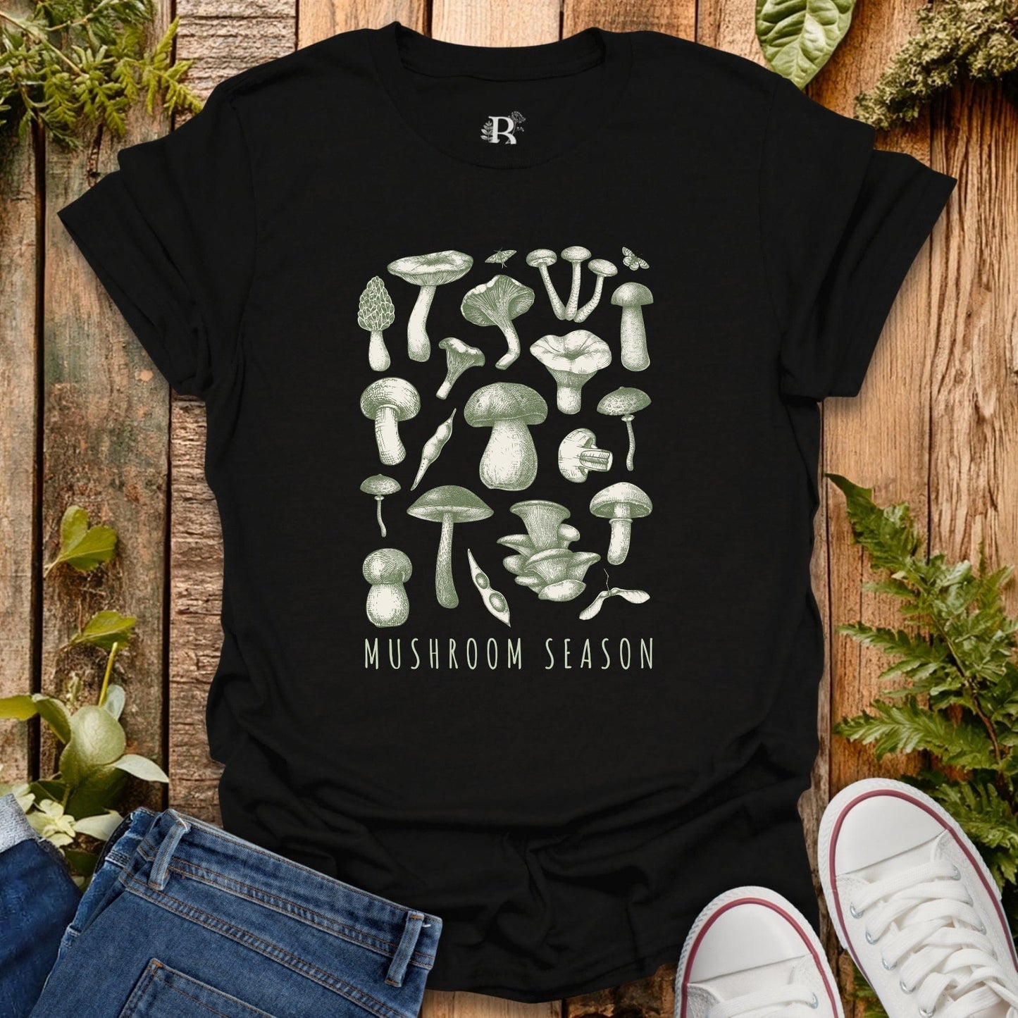 Black t-shirt with mushroom graphic and 'Mushroom Season' text on a wooden surface with plants.