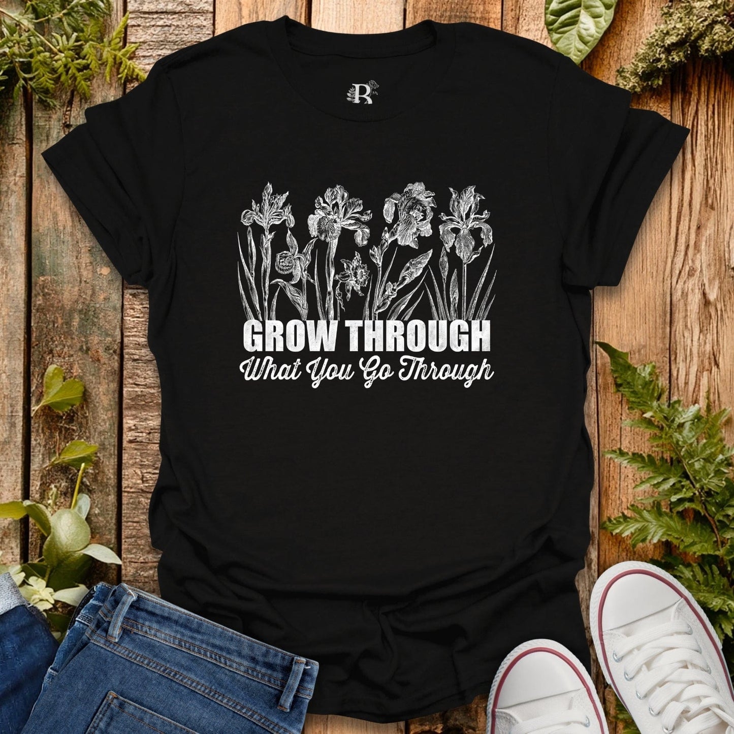 Black t-shirt with white floral design and text on a wooden surface with plants.