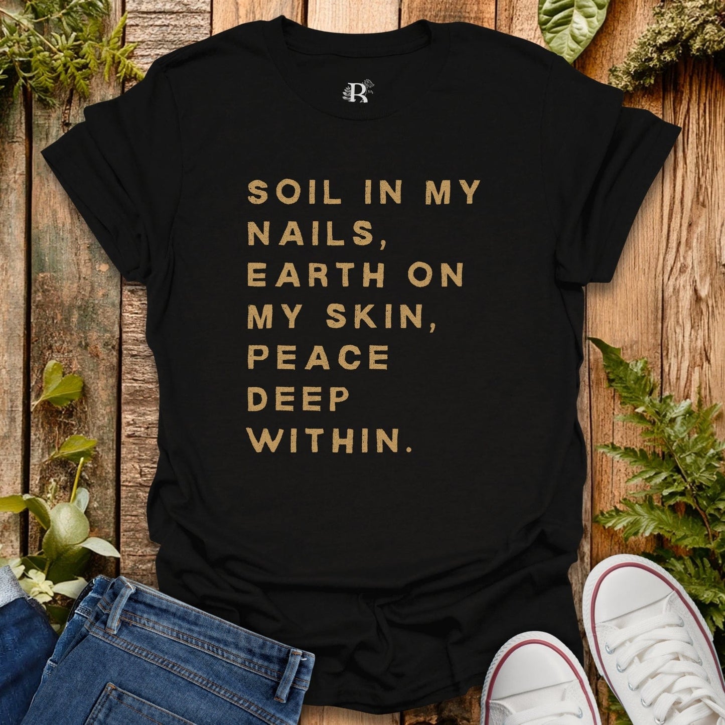 Black t-shirt with gold text on a wooden surface with plants