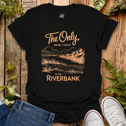 Black t-shirt with a scenic design and text on a wooden surface with plants.