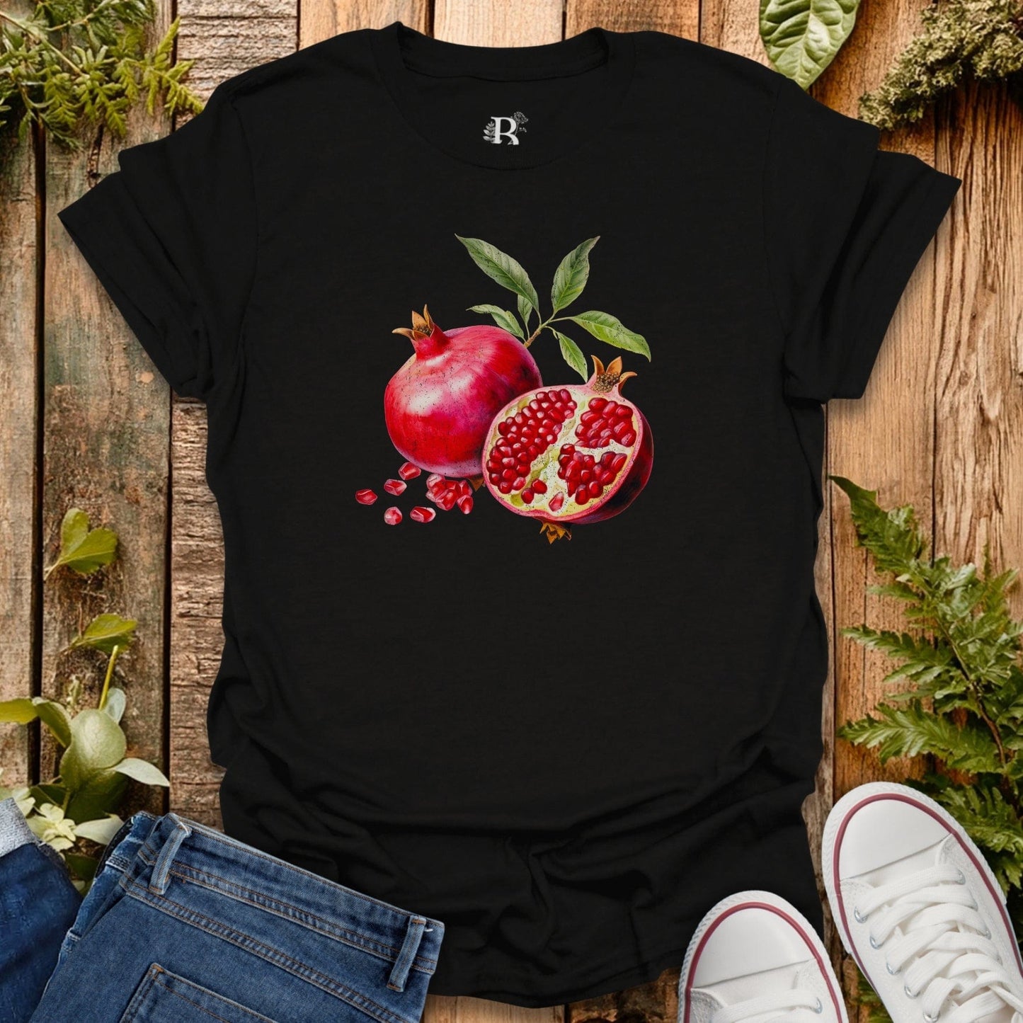 Black t-shirt with pomegranate design on a wooden surface with jeans and shoes.