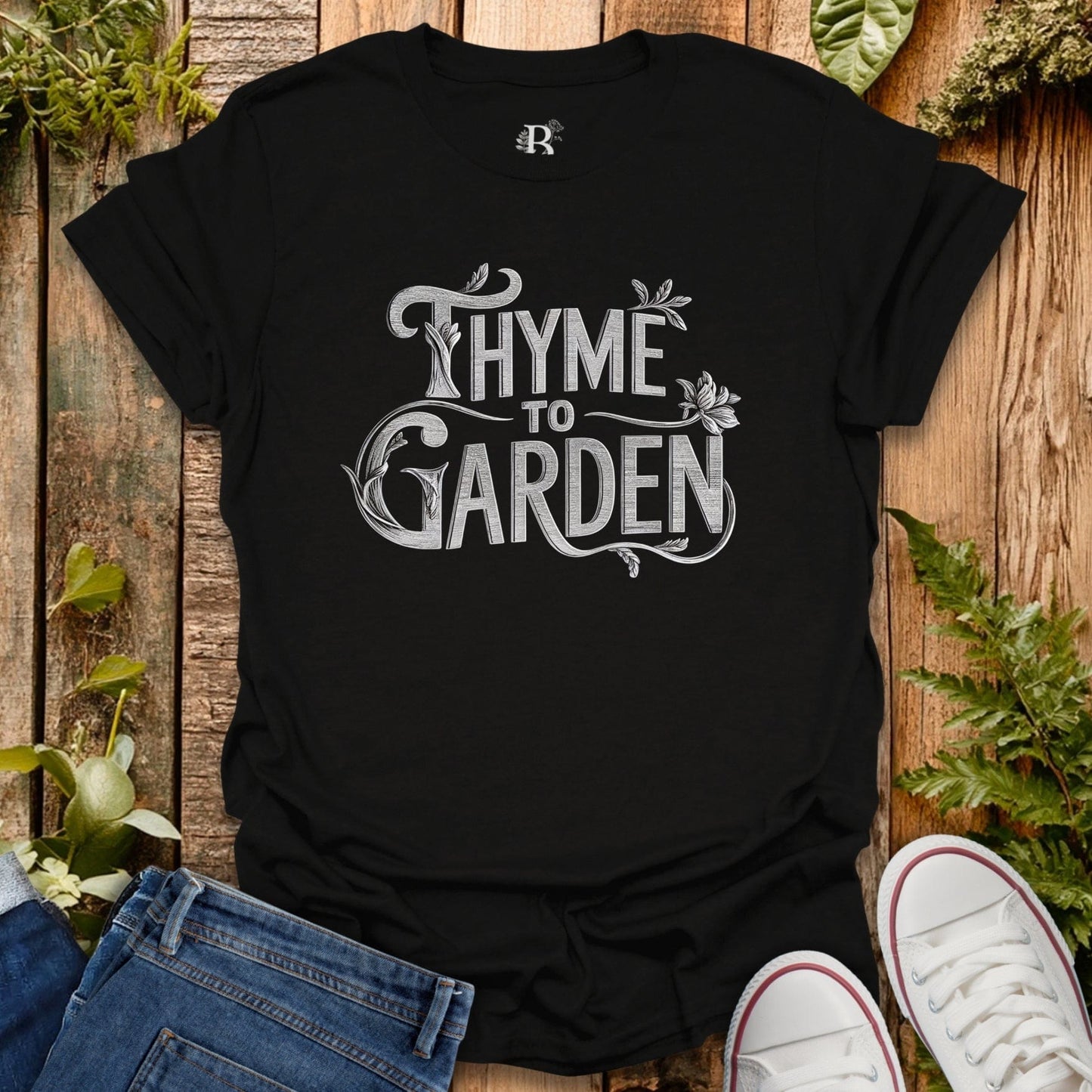 Black t-shirt with 'Thyme to Garden' text on a wooden surface with plants.