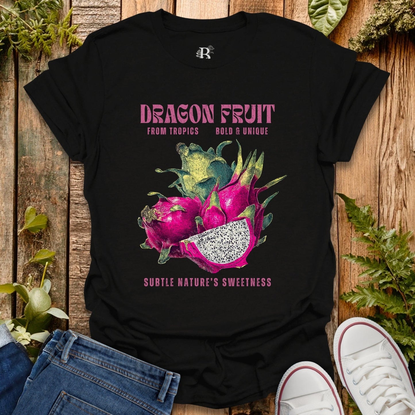 Black t-shirt with dragon fruit graphic and text on a wooden surface with plants.