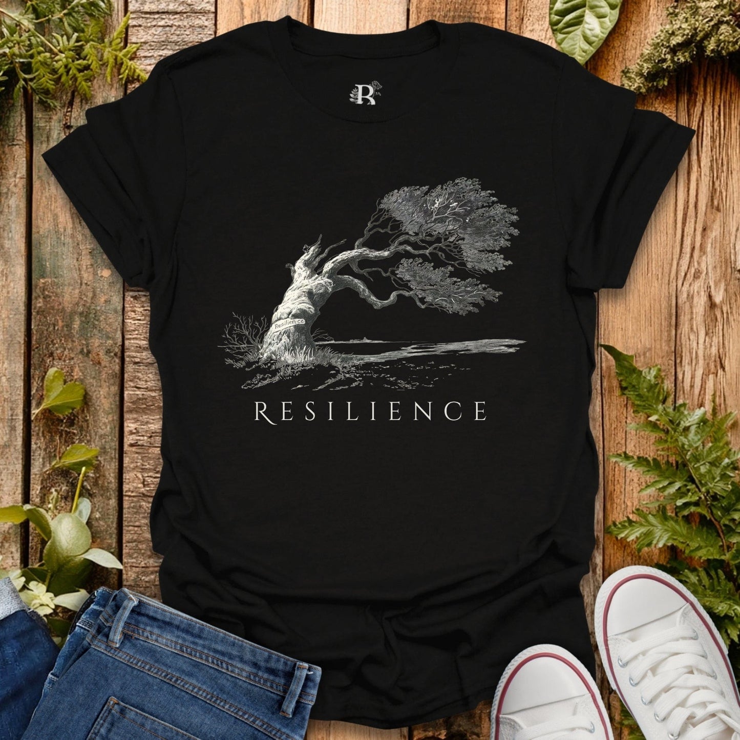 Black t-shirt with 'Resilience' graphic design on a wooden surface with plants.