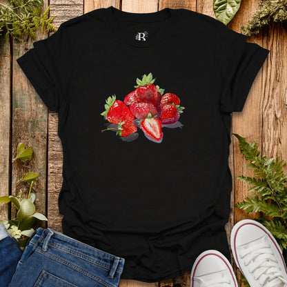 Black t-shirt with strawberry design on a wooden surface with jeans and shoes.